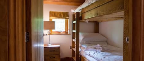 A compact bedroom with a bunk bed, a bedside table with a lamp, and a window with a curtain.