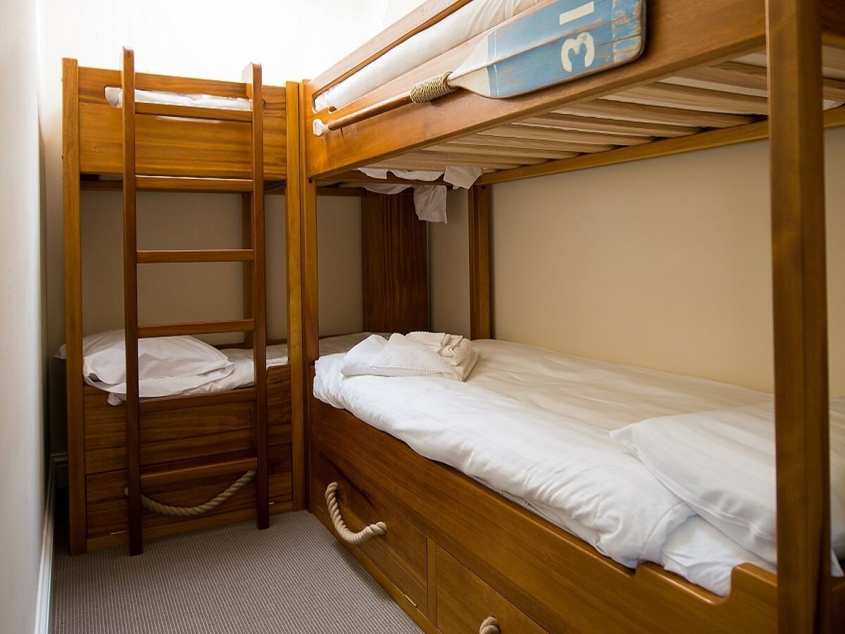 A bunk bed room with a ladder, a small desk, and a storage drawer.