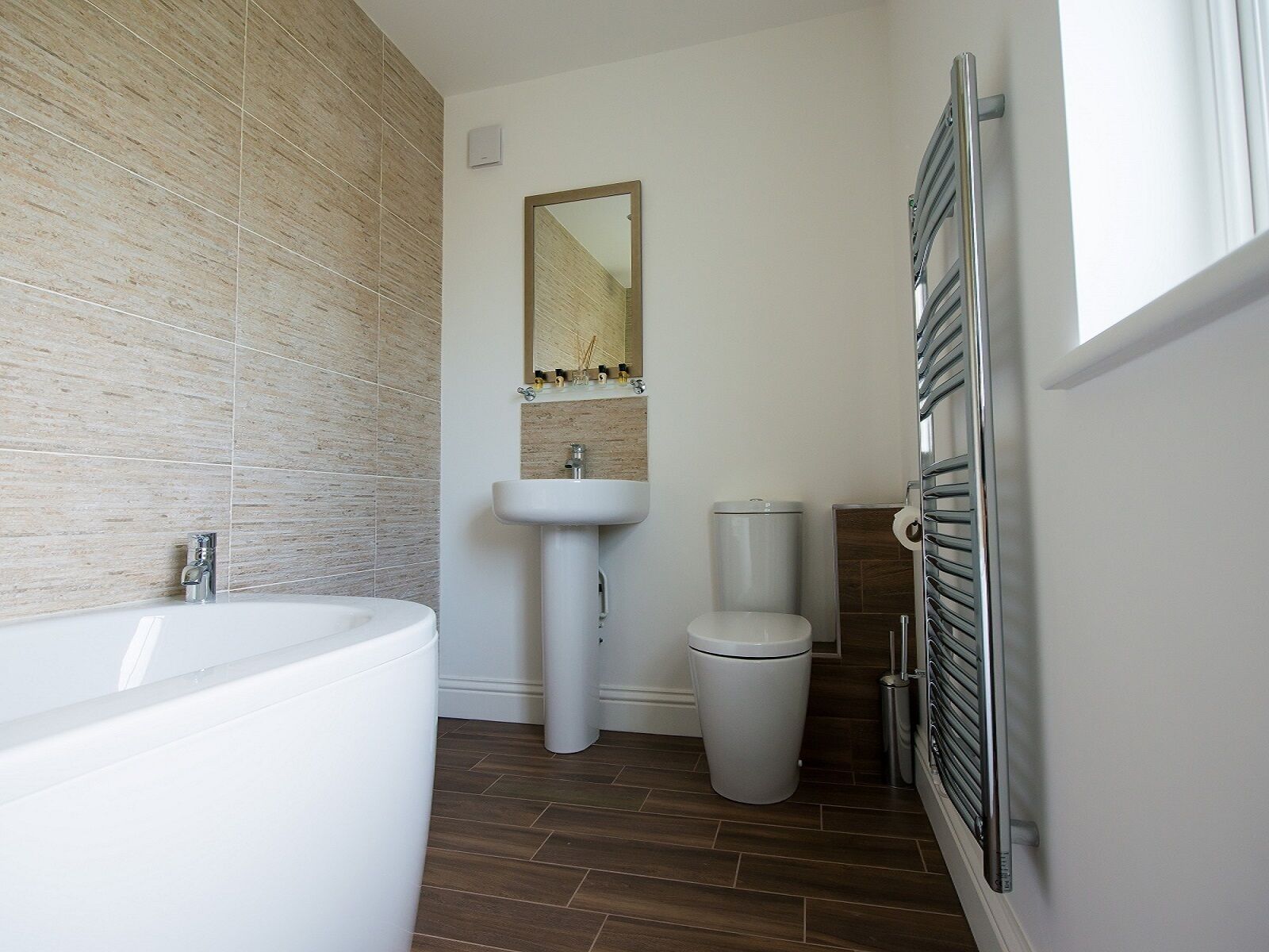 Un baño moderno con una bañera blanca grande, un lavabo pedestal, un inodoro y un perchero para toallas.