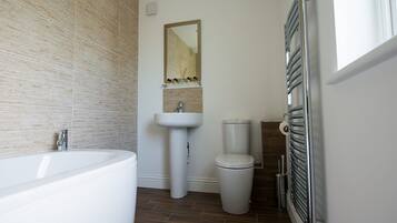 Un baño moderno con una bañera blanca grande, un lavabo pedestal, un inodoro y un perchero para toallas.