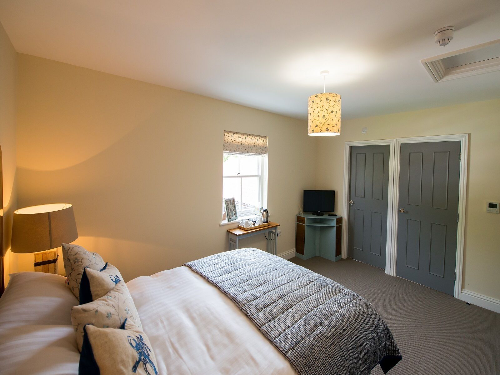 A bedroom with a bed, a desk, a television, and two doors.