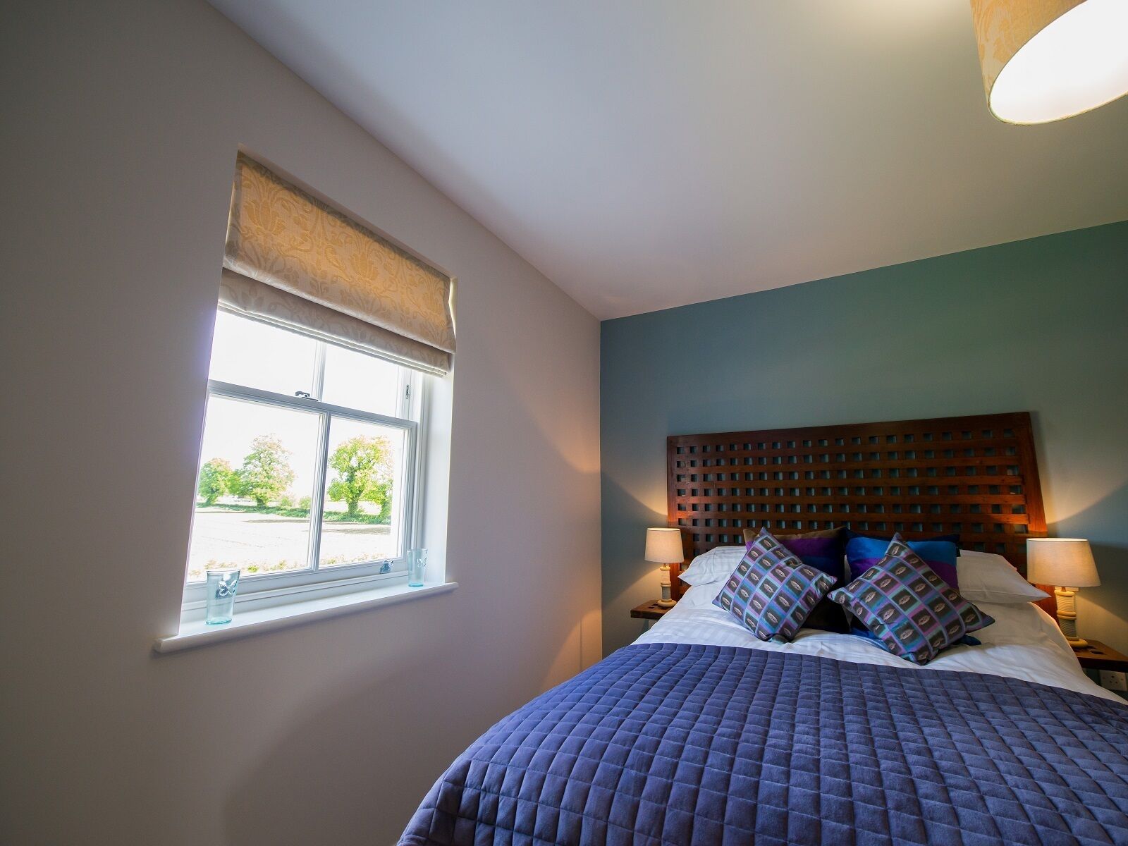A bedroom with a bed, two bedside tables, a window with a view, and a headboard with a grid pattern.