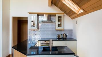 A modern kitchen with a black countertop, white cabinets, and a wooden ceiling.