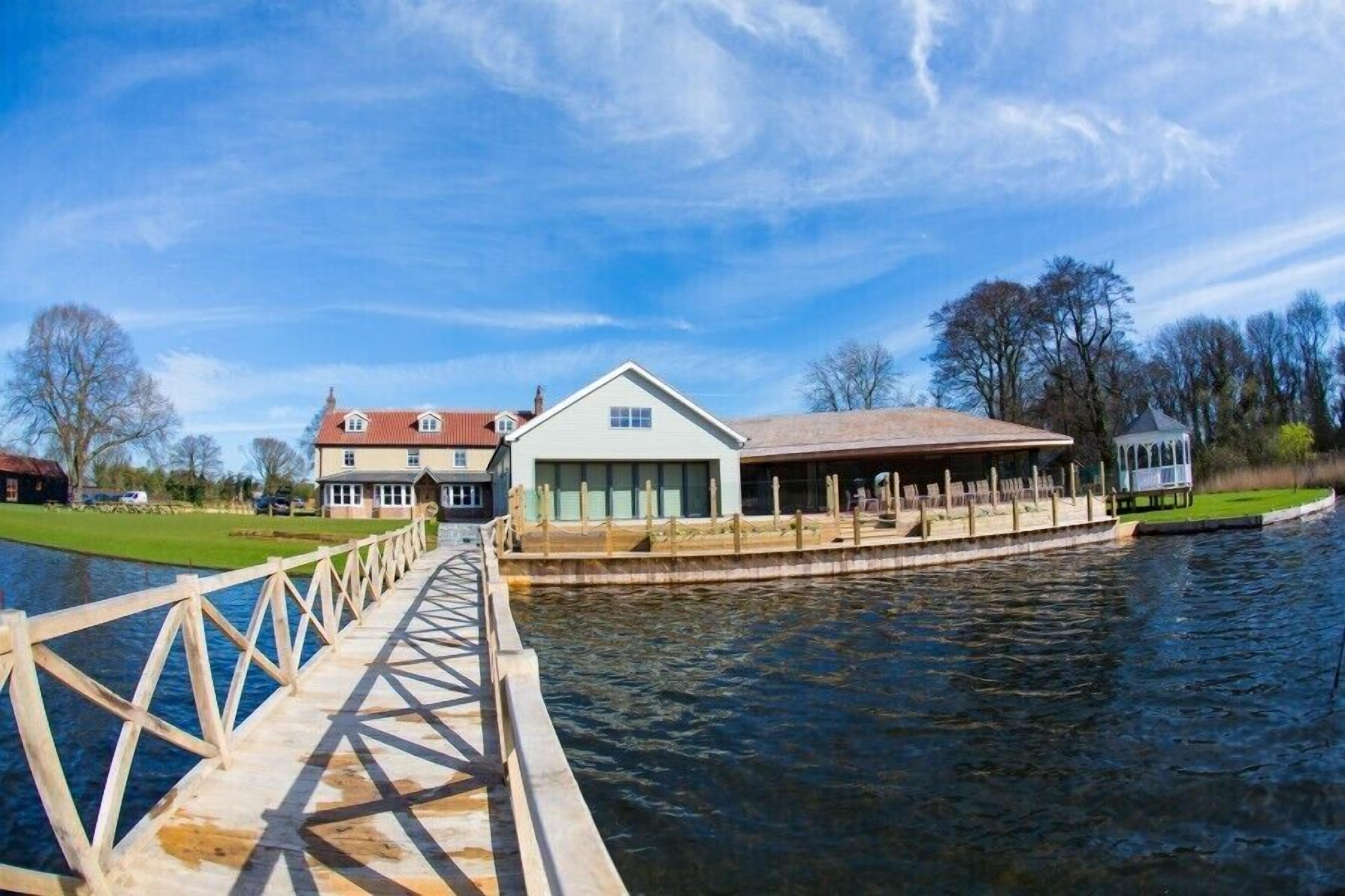A wooden bridge leading to a waterfront property with a large house and a covered area.