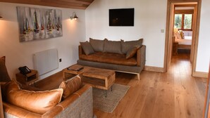 A cozy living room with a brown leather sofa, a wooden coffee table, and a painting of sailboats on the wall. - The Boathouse (Great Yarmouth)