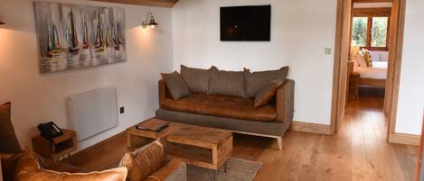 A cozy living room with a brown leather sofa, a wooden coffee table, and a painting of sailboats on the wall.