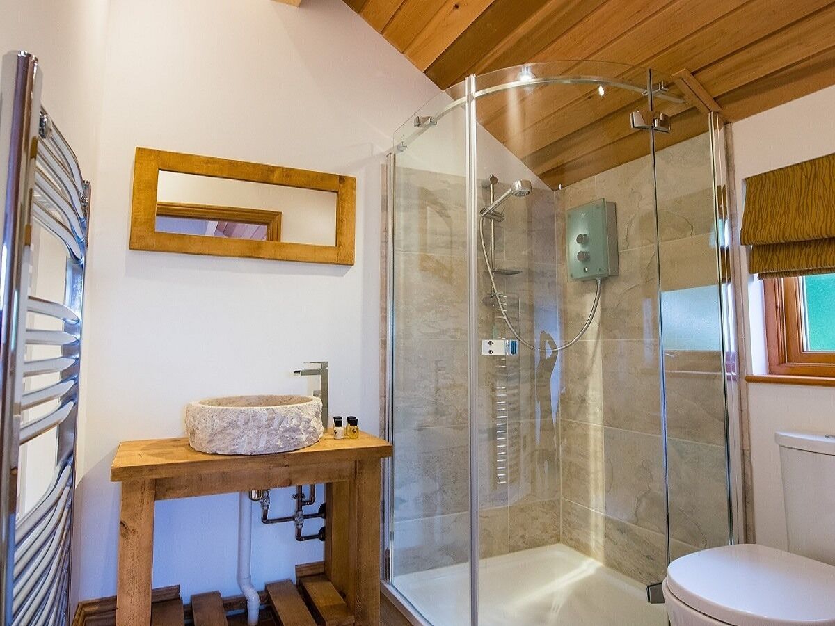 Ein modernes Badezimmer mit einer gläsernen Duschkabine, einem hölzernen Waschtisch mit Steinbecken und einer Toilette.