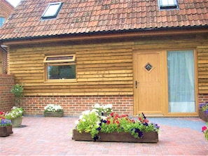 A wooden log cabin with a tiled roof, a wooden door, and a window. There are flower planters in front of the cabin.
