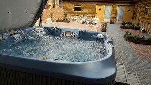 Een hottub in een open omgeving met een terras van baksteen, witte stoelen en potplanten.