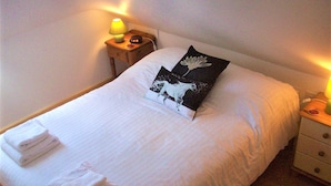 Een net opgemaakt bed met witte lakens, twee kussens en een bedlampje op een houten nachtkastje.