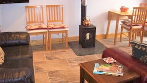 Een woonkamer met een open haard, twee houten stoelen, een bank, een tafel met tijdschriften en een televisie aan de muur.