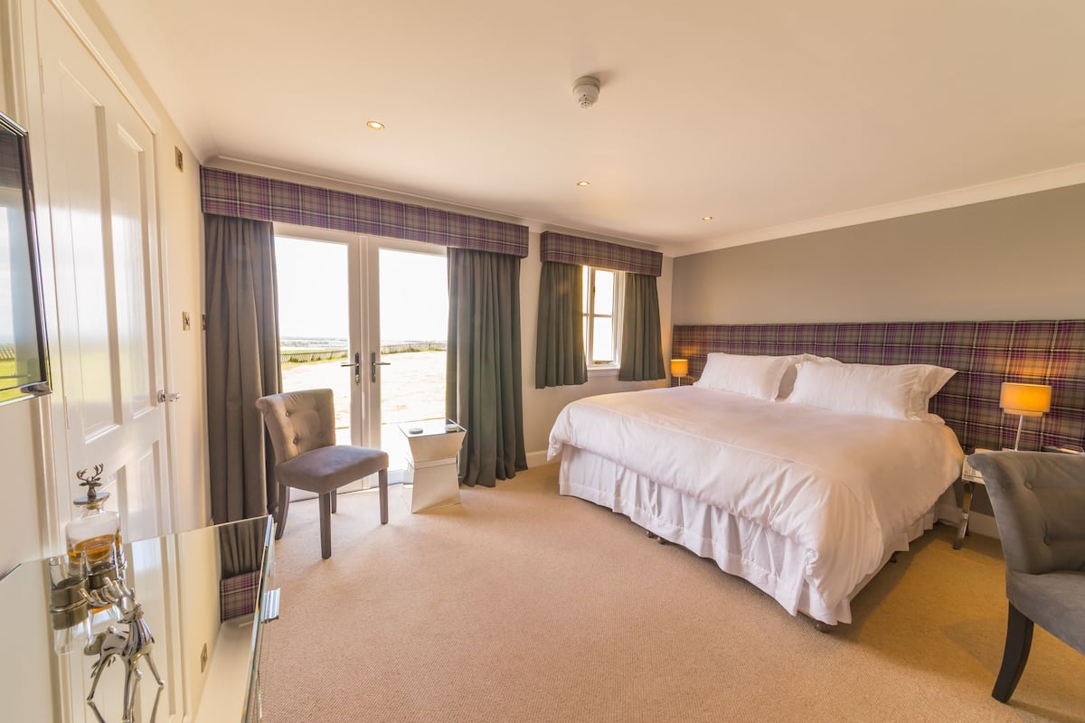 Habitación de hotel con una cama grande, dos sillas, un escritorio y vista a la playa.