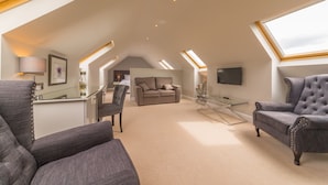 A spacious loft with high ceilings, a cozy seating area with a sofa and chairs, a flat-screen TV mounted on the wall, and skylights providing natural light. - Garleton Lodge (Haddington)