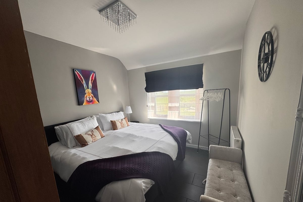 Un dormitorio con una cama, una silla, un radiador, una ventana y un reloj de pared.