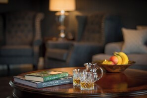 A room with a round wooden table, a bowl of fruit, two books, and a glass pitcher.