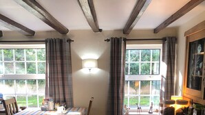 A cozy dining area with a wooden table and chairs, a kitchen counter with various items, and large windows with curtains. - Elm Tree Farm Bed & Breakfast (Withernsea)