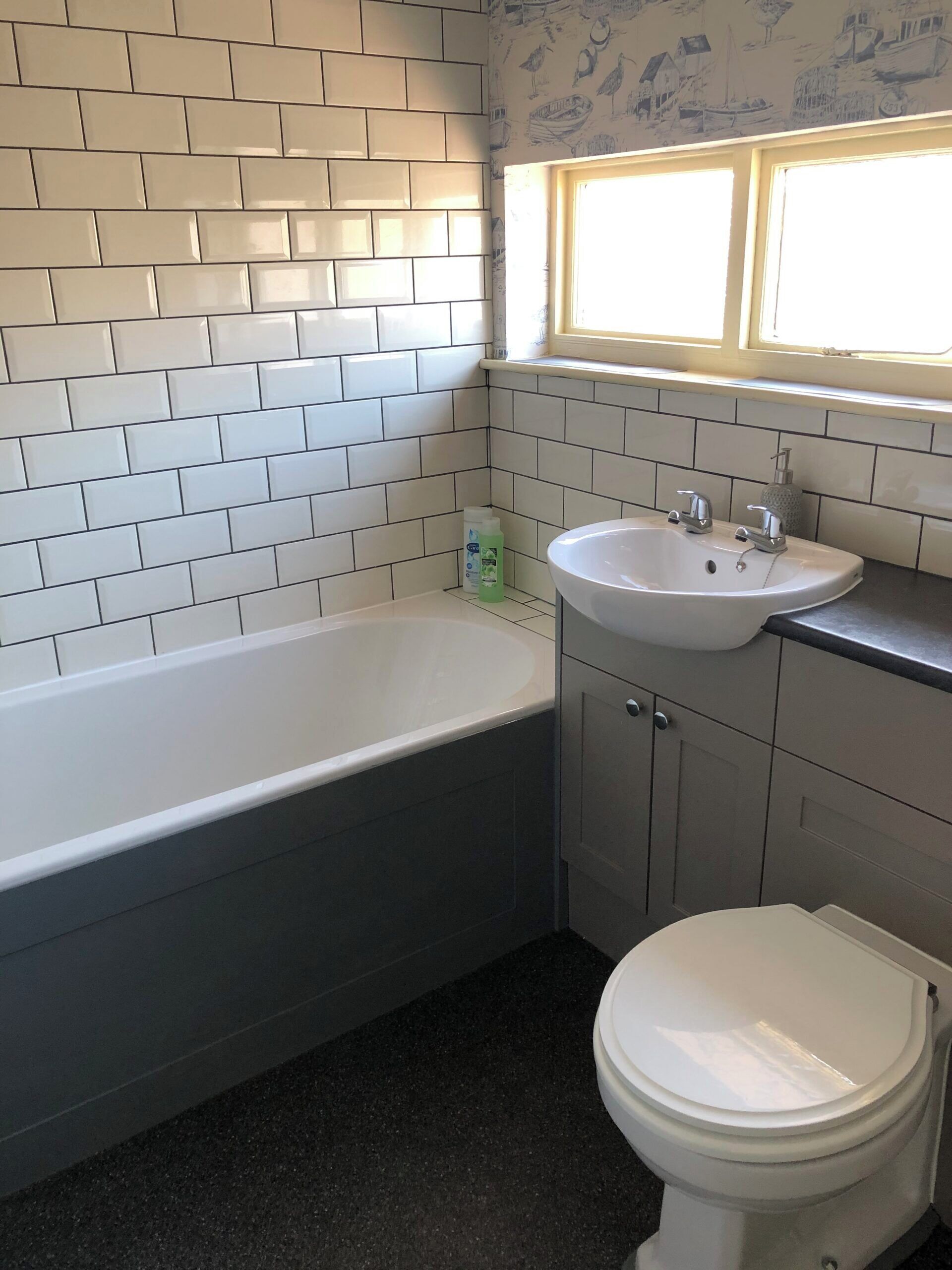 Un baño con pared de azulejos blancos, una bañera, un lavamanos y un inodoro.
