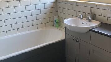Un baño con pared de azulejos blancos, una bañera, un lavamanos y un inodoro.