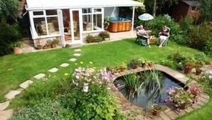 A house with a covered patio, a hot tub, and a small pond with surrounding plants. - Elm Tree Farm Bed & Breakfast (Withernsea)