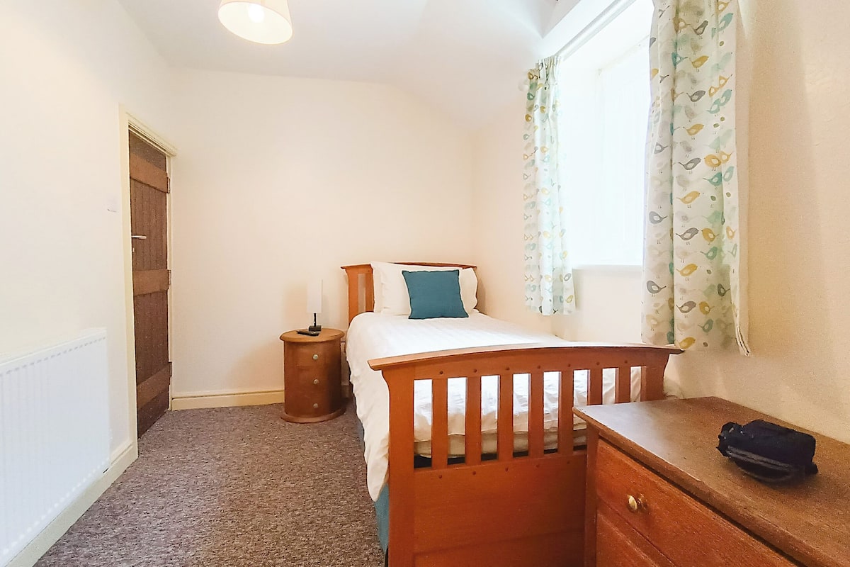 A bedroom with a bed, bedside table, lamp, and a window with curtains.