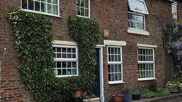 A brick house with ivy-covered walls, multiple windows, and a small garden area with potted plants.