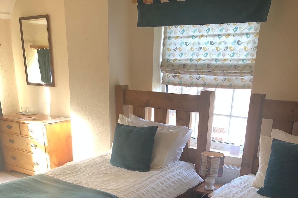 A room with two wooden beds, a dresser, a mirror, and a window with patterned curtains.