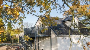 A modern house with a balcony, a covered porch, and a small garden area. - Dunroamin Apartment (Glasgow)