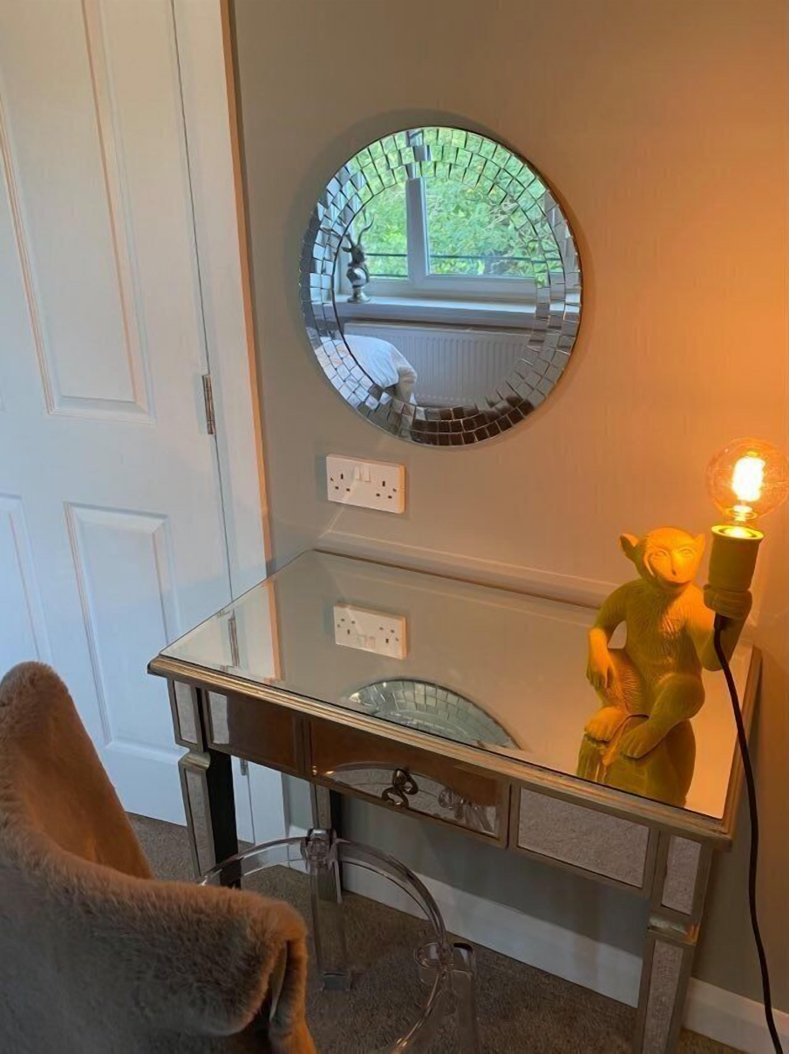 Une salle de bain avec un meuble-lavabo en verre, un miroir rond, un luminaire et un porte-serviettes.