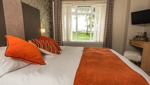 A hotel room with a large bed, a desk with a chair, a flat-screen TV, and a window with curtains. - Dunroamin (Glasgow)