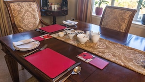A dining table set with red placemats, white plates, silverware, and a patterned table runner. - Dunroamin (Glasgow)