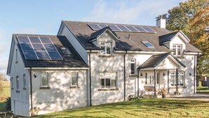 A two-story house with solar panels on the roof, a well-maintained lawn, and a bench in the front yard. - Dunroamin (Glasgow)