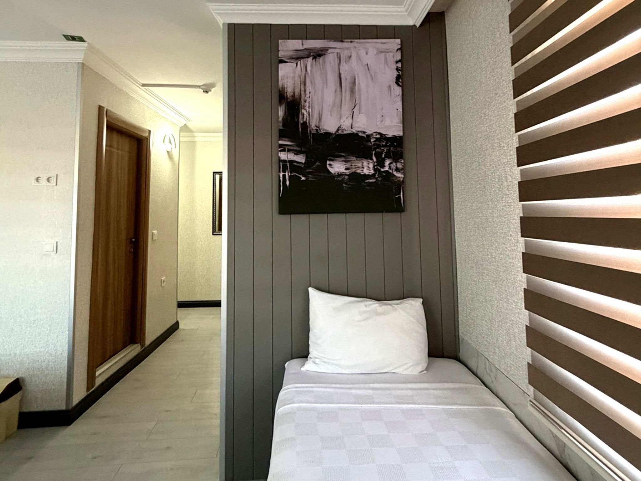 A hotel room with a bed, a painting on the wall, and a window with blinds.