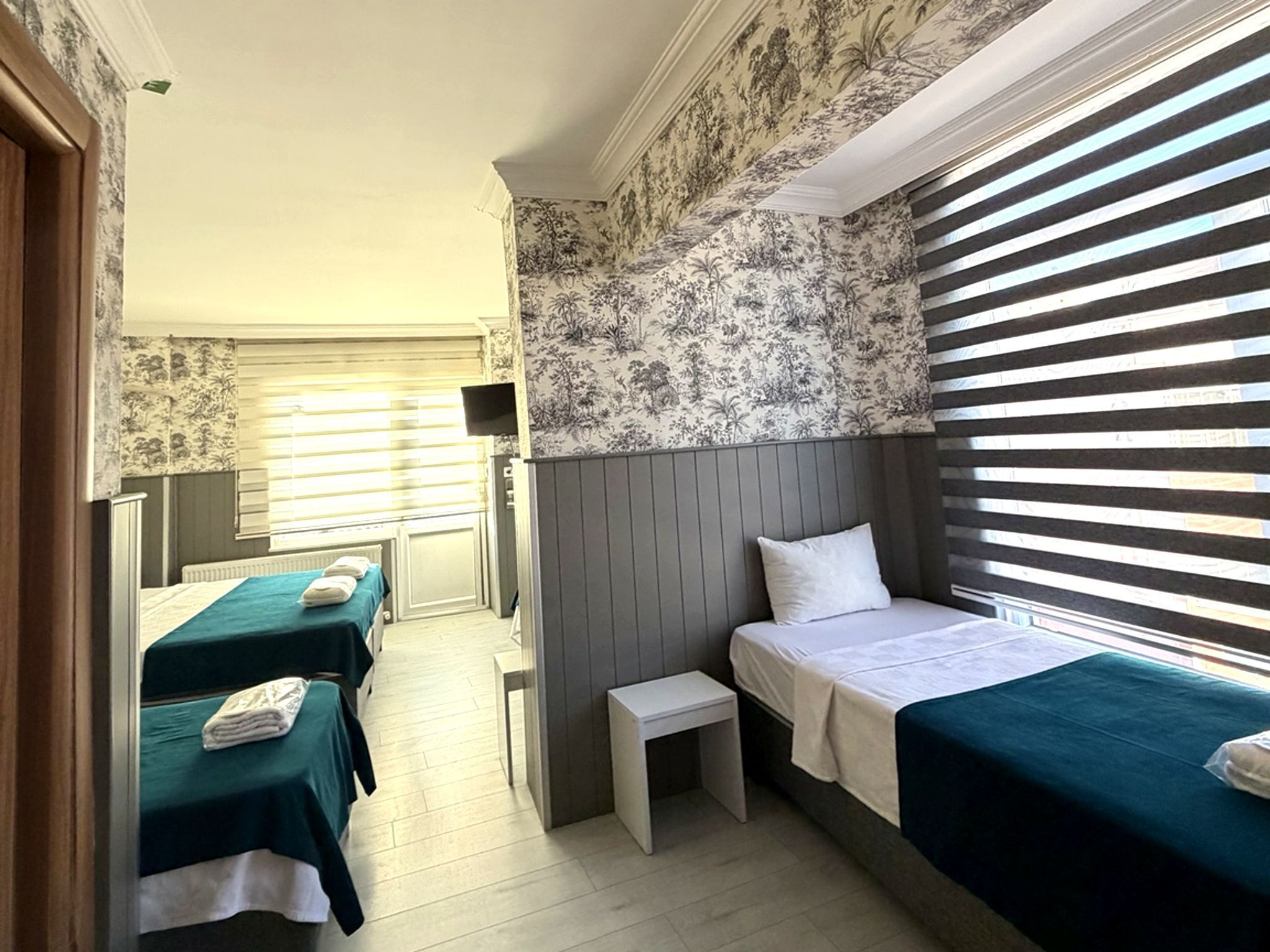 A hotel room with two single beds, a small table, and a window with blinds.