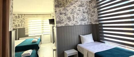 A hotel room with two single beds, a small table, and a window with blinds.
