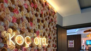 A hotel reception area with a wall of artificial flowers and a neon sign reading "KOC OTEL". - Koc Hotel (Karasu)