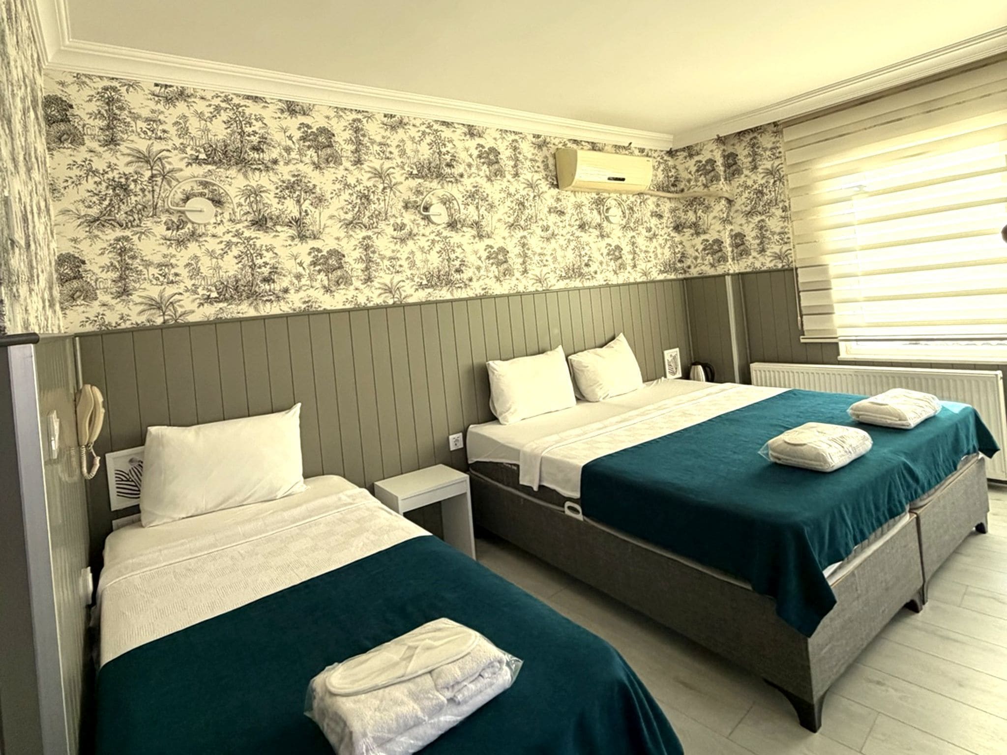 A hotel room with two beds, a telephone, a radiator, and a window with blinds.