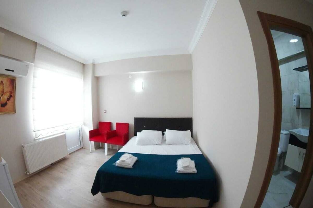A hotel room with a bed, a red chair, a white radiator, and a window.