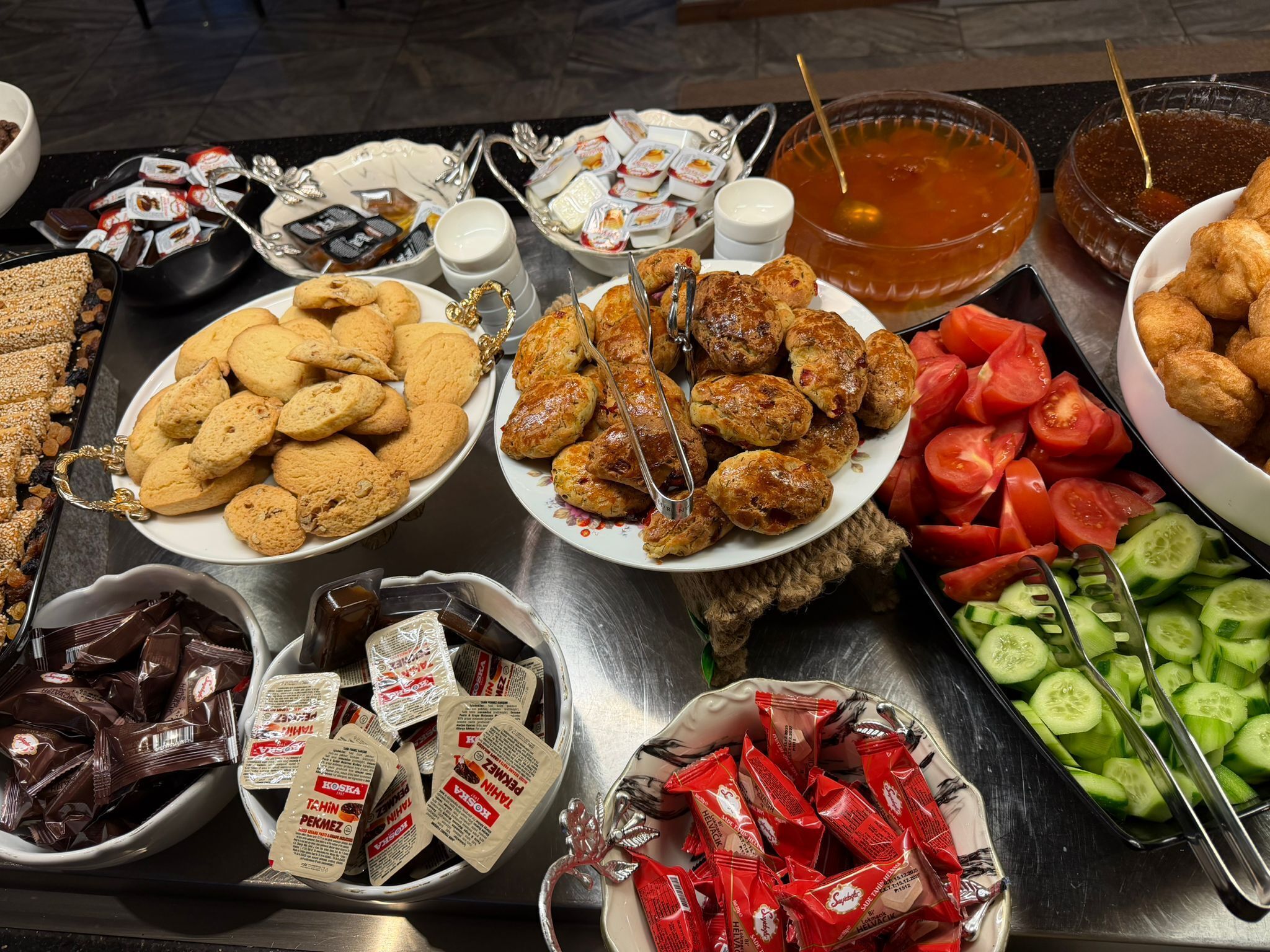 A buffet with various food items including cookies, scones, and sliced vegetables.