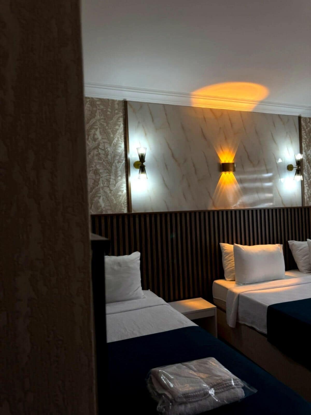 Een hotelkamer met twee bedden, een houten hoofdbord en wandlampen.