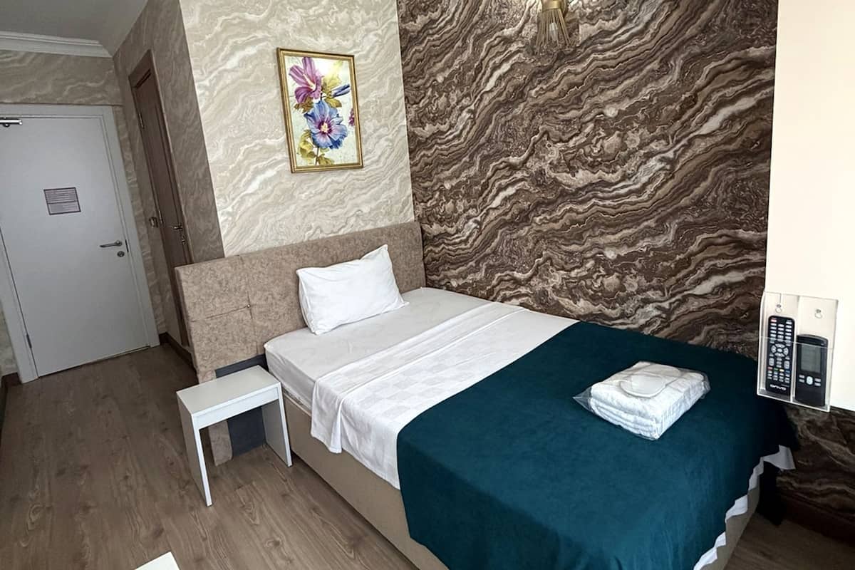 A hotel room with a bed, bedside table, and a painting on the wall.