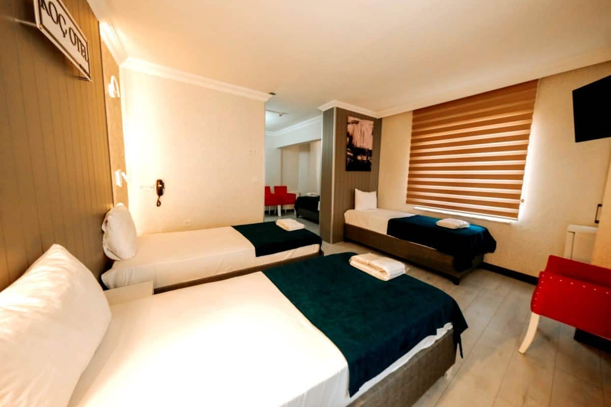 A hotel room with two single beds, a desk, a chair, a TV, and a window with blinds.