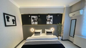 A modern hotel room with a large bed, a bedside table, a potted plant, and artwork on the walls. - Koc Hotel (Karasu)