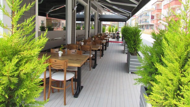An outdoor cafe with wooden tables and chairs, potted plants, and a covered walkway. - Koc Hotel (Karasu)
