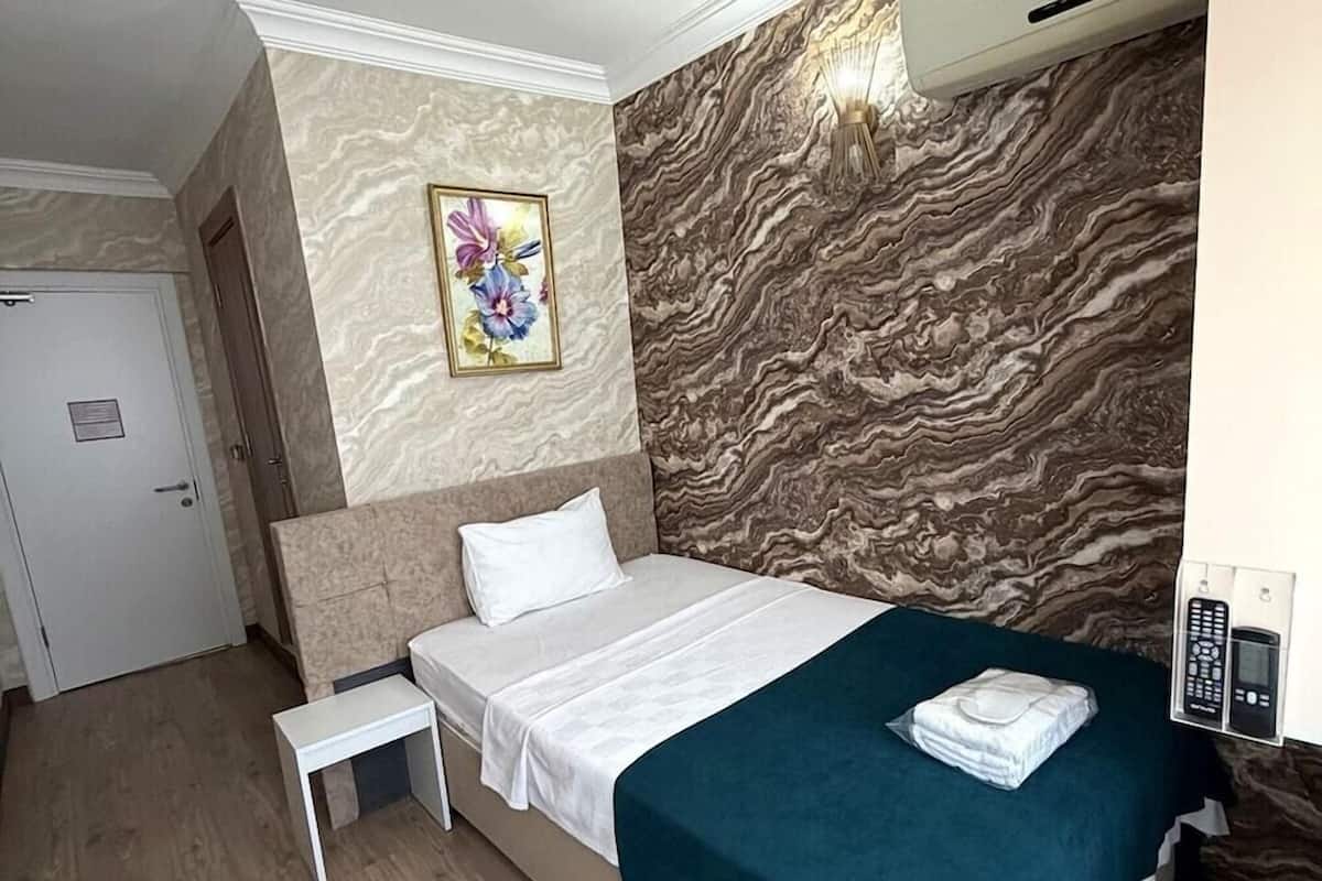 A hotel room with a bed, a bedside table, a wall-mounted painting, and a marble-patterned wall.