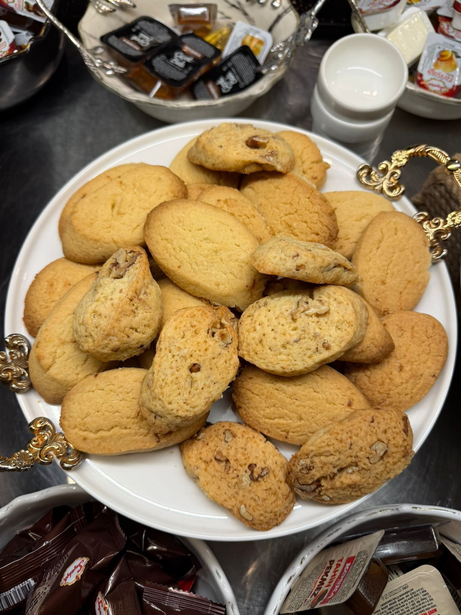 Un plato de galletas con nueces, un vaso de leche y algunas barras de chocolate sobre una mesa.