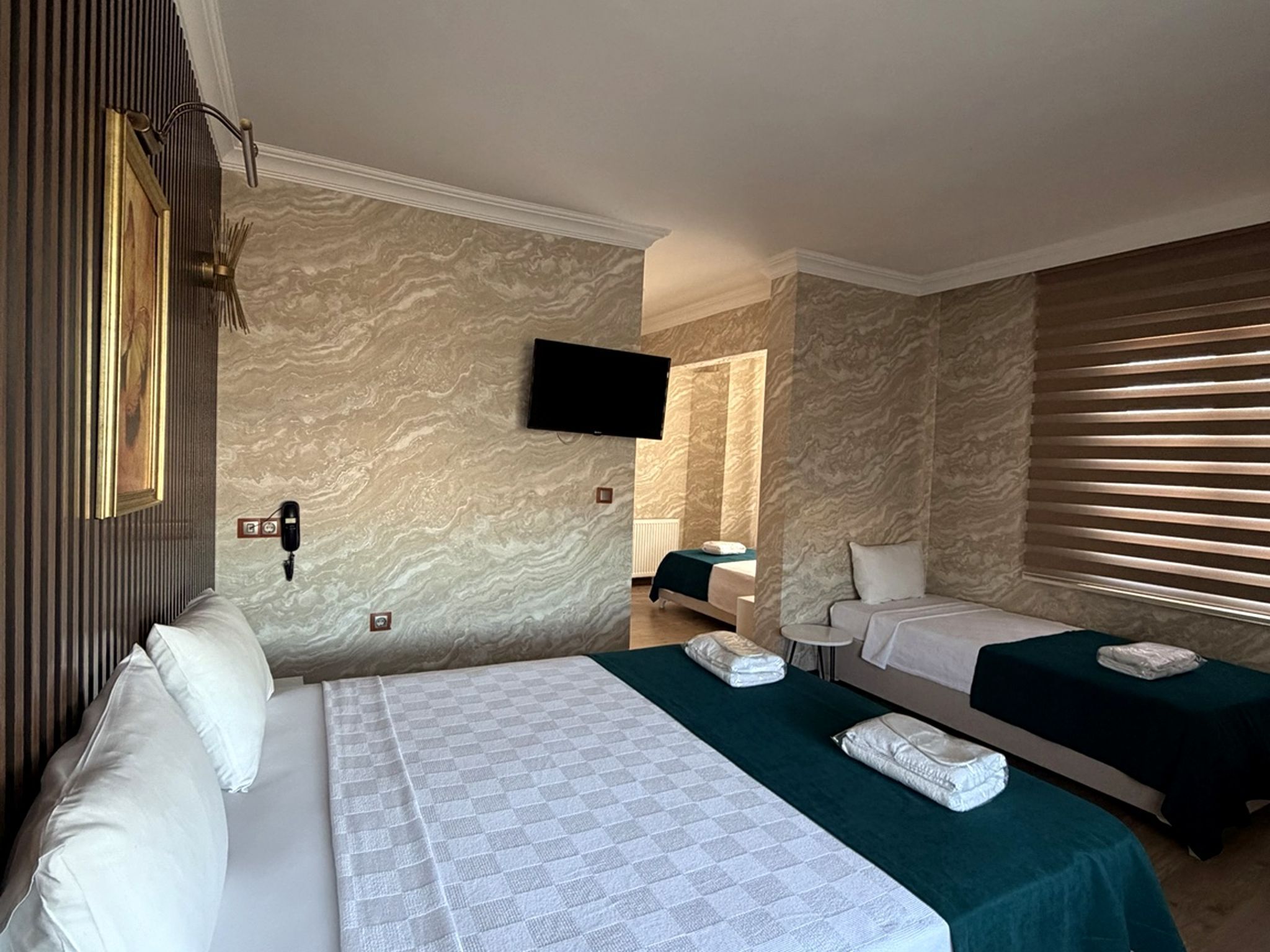 A hotel room with a large bed, two smaller beds, a TV, a phone, and a window with blinds.