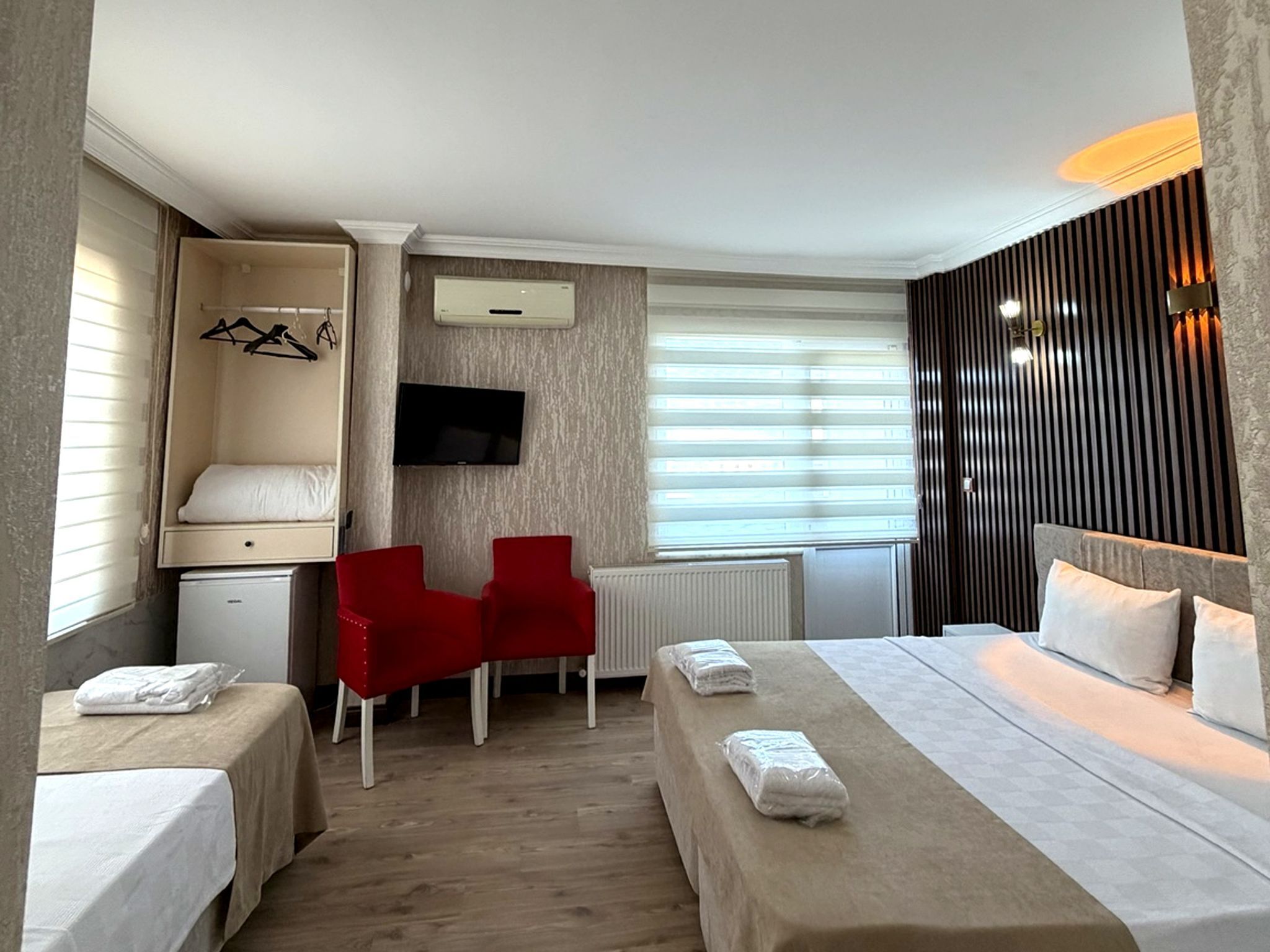 Ein Hotelzimmer mit einem Bett, zwei Nachttischen, einem Schreibtisch mit Stuhl, einem Fernseher und einem Fenster mit Jalousien.