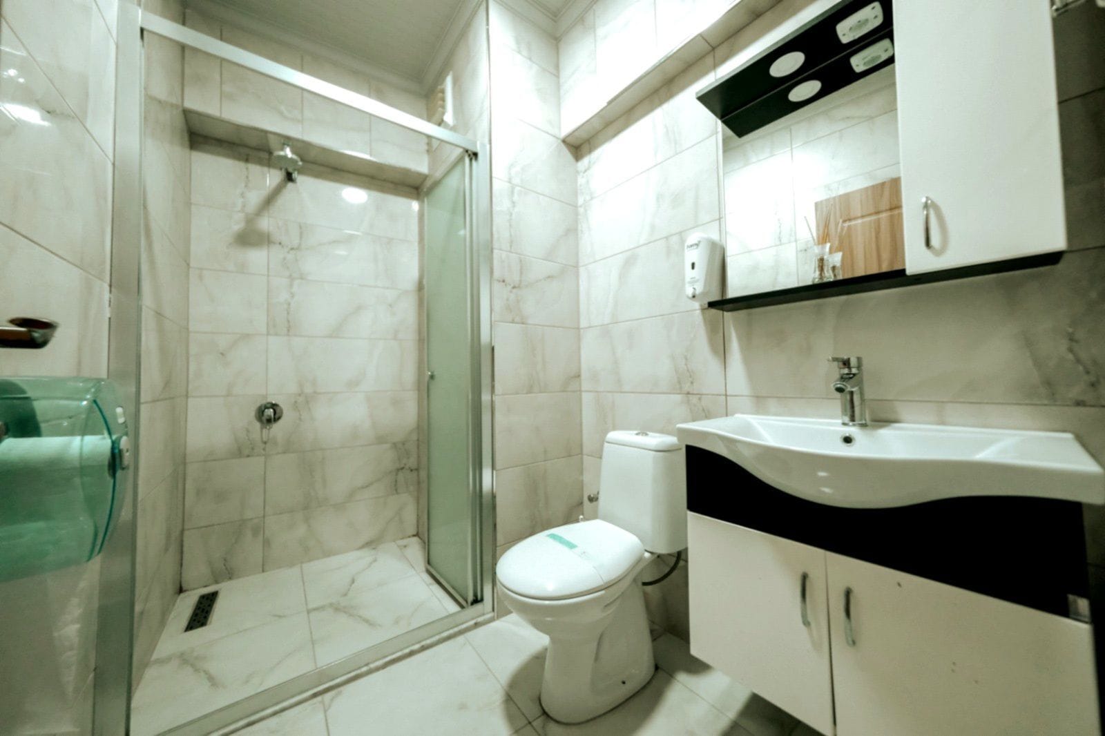Un baño moderno con ducha envuelta en vidrio, inodoro y lavamanos con encimera negra.