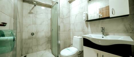Un baño moderno con ducha envuelta en vidrio, inodoro y lavamanos con encimera negra.