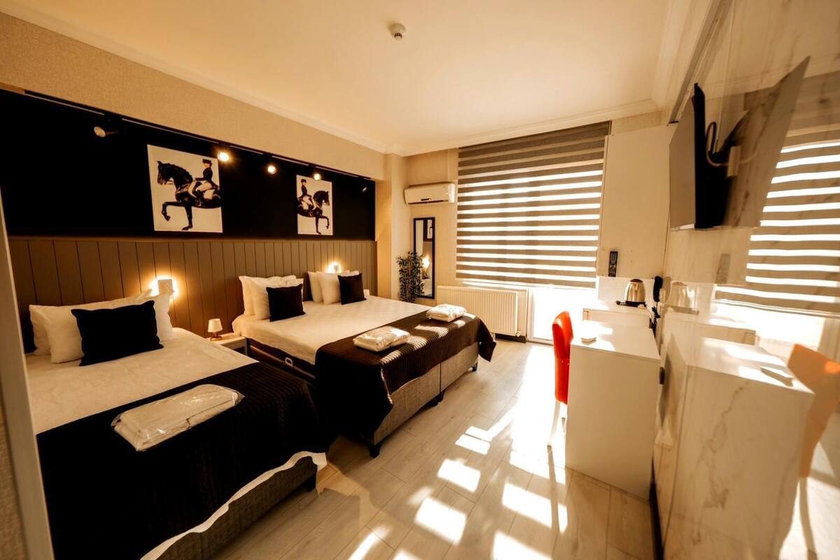 A hotel room with two beds, a desk, and a window with blinds.